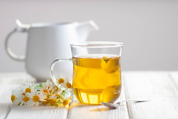Cup of herbal tea with chamomile flowers on the white wooden background. Natural organic alternative medicine concept