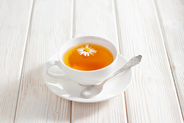 White cup of herbal tea with chamomile flowers on the white wooden background. Natural organic alternative medicine