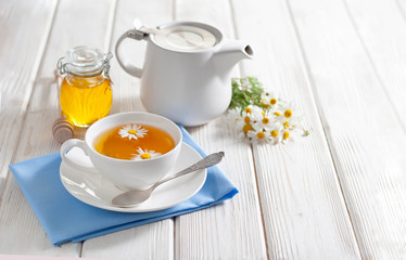 Cup of herbal tea with honey and chamomile flowers on the white wooden background. Natural alternative medicine