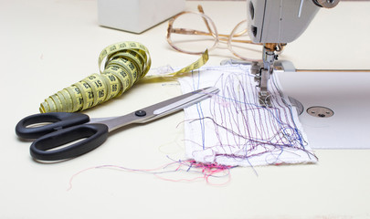 Sewing machine with a needle, next to a scissor and a tape for measuring.
