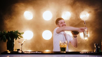 Attractive bartender professionally juggling cups and doing a show in beautiful modern bar. Slow motion