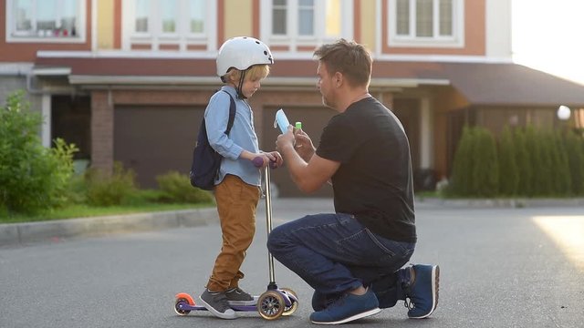 Child with scooter going to school after covid-19 quarantine and lockdown. Father giving son face mask and sanitizer.It is new normal for protection and prevention while outbreak of coronavirus or flu
