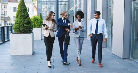 Mixed-races young cheerful people in business style walking the street , laughing and talking....