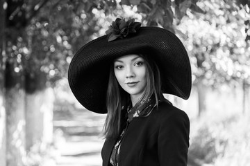 Red-haired girl in a big hat with red flower fields on a green alley in a summer park