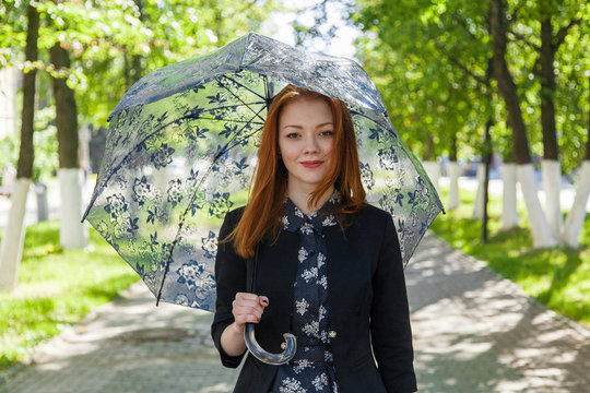 Red-haired girl with a lace umbrella walks along the green alley and laughs