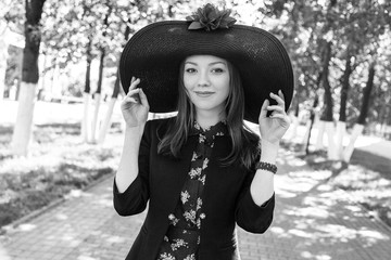 Red-haired girl in a big hat with red flower fields on a green alley in a summer park