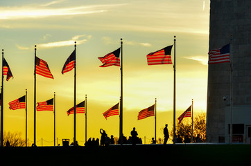 Washington Monument and silhouettes and waving national flags during sunset - Washington D.C....