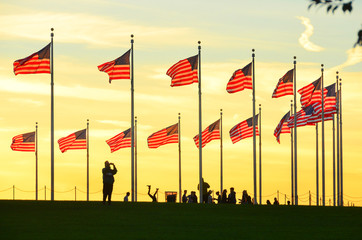 Washington Monument and silhouettes and waving national flags during sunset - Washington D.C....