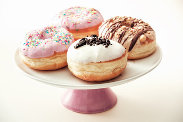 Various chocolate donuts, served on top of dessert plate, isolated against pastel background.