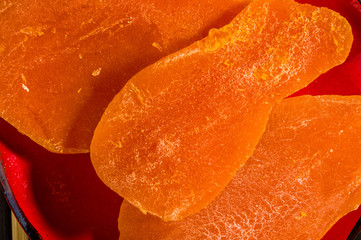 Slices of dried mango in a red saucer on a bamboo mat, closeup.