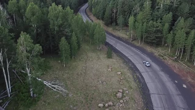 Aerial video of silver car on a mountain road through a forest