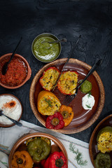 Vegan stuffed peppers with rice, corn grits, vegetables and herbs on clay servingware with side dishes, copy space