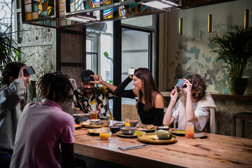Teenage friends sitting at the cafe and playing a word-guessing game with the help of their smartphones.