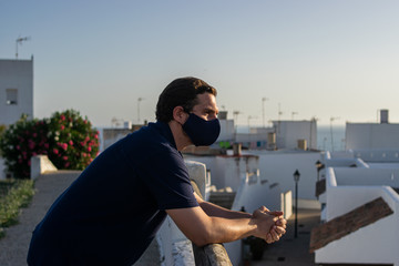Photo of a young and attractive man wearing a face mask enjoying the views of Conil. White houses, doing tourism during coronavirus outbreak. Social distance and isolation