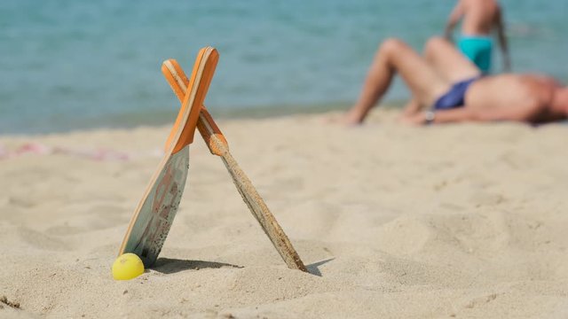 Two rackets and ball are on blue sea background and relaxing tourist. Matkot on the sandy beach. Beach tennis, paddle. Vacation on sea. Active healthy lifestyle. Catalonia, Spain.