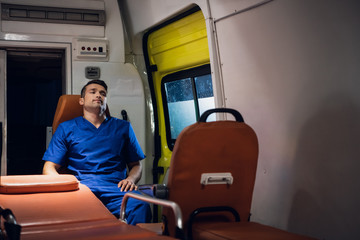 Medical worker sitting in an ambulance car, having a rest, meditating.