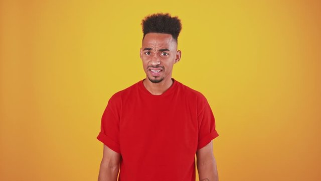 Young black man feeling aversion and shock, raising hands and refusing, orange studio background