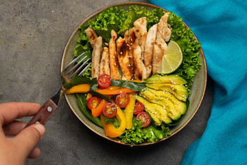 Grilled chicken salad with avocado and vegetables on dark background