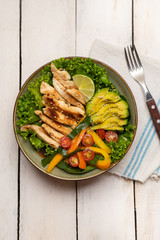 Grilled chicken salad with avocado and vegetables on white background
