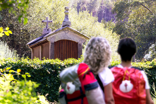 way to Santiago of Compostela , women couple pilgrims unfocused with  scallop shell sign  in english route , near Mino village , Coruna , Spain