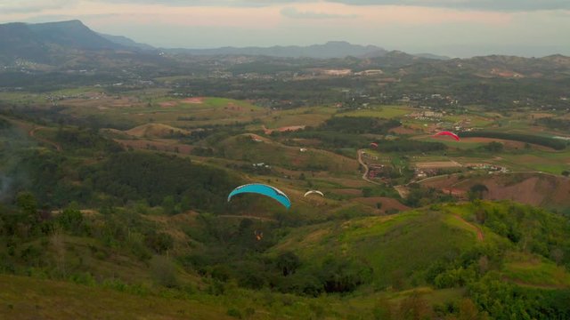 Three paragliders fly over mountain top in sunset light. Parachutes or paragliding experience. Adrenaline and extreme sport.