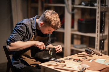 a young man is engaged in the family craft of making leather shoes in a workshop - Powered by Adobe