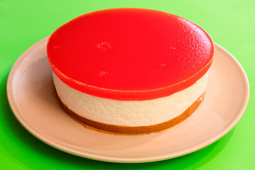 Homemade cheesecake with watermelon jelly on the top, on a bright contrasting green background (close-up photo, selective focus)