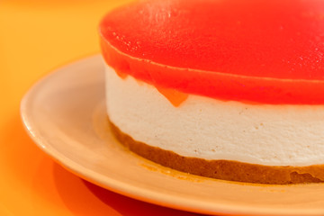 Homemade cheesecake with watermelon jelly on the top, on a bright orange background (macro photo, selective focus)