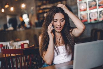 Business woman talking to the phone, working on a laptop and drinking coffee in a cafe.