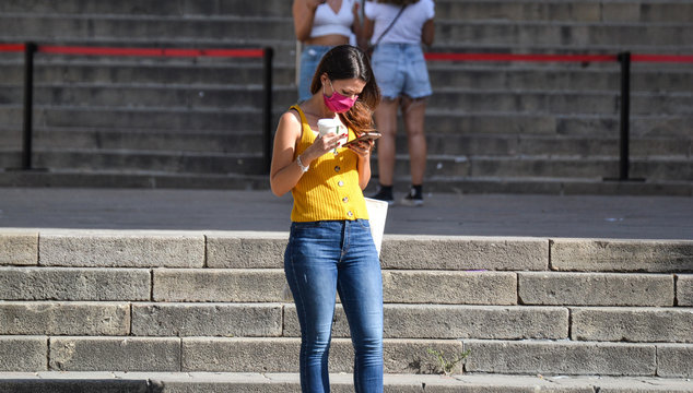 Barcelona, Spain, August 24, 2020: Caucasian woman wearing protective covid-19 face mask while checking her phone. Touristy spots in the covid era