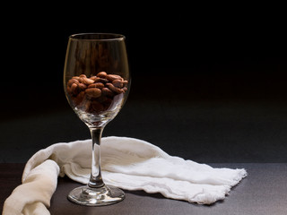 Copa de vino rellena de semillas de cacao  en un fondo negro con una manta blanca de decoración