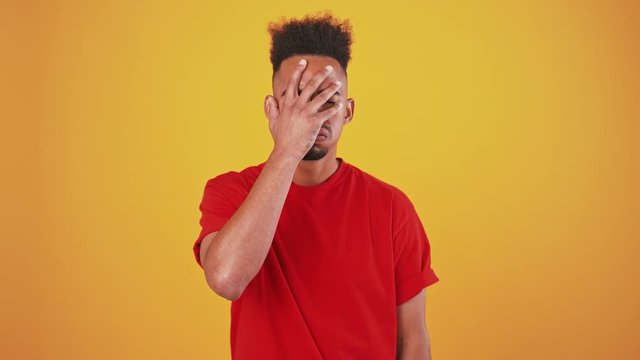 Displeased young man man showing facepalm gesture, orange background