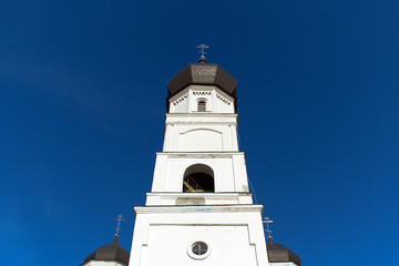 bright white central tower of orthodox cathedral with cross on blue sky background