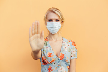 Hand stop sign. Woman in a sterile medical mask on her face, shows stop hand gesture for stop coronavirus outbreak. The concept of preventing the spread of the pandemic. Stop the virus.