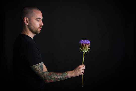 Portrait of young man holding purple artichoke flower on black background, greeting card or concept