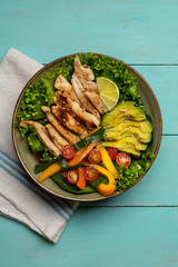 Grilled chicken salad with avocado and vegetables on turquoise background
