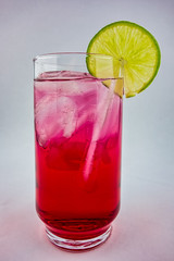 Red drink with ice and lemon slice on the edge of the glass on white background