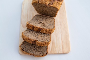 Composition in the rays of the bright sun. Homemade whole grain rye bread (with sesame seeds), cut into slices on a wooden board. On a light background