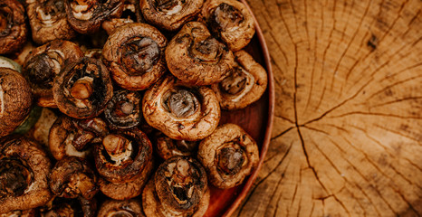 Cooked baked champignon mushrooms lie on a brown clay plate on a cracked brown hemp. Summer green blurred grass background.