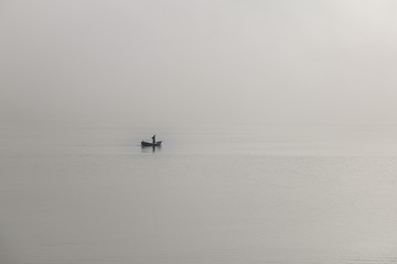 Fototapeta na wymiar Homem navegando num pequeno barco com mar e céu encobertos pela névoa