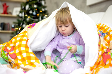 Fototapeta na wymiar christmas morning, little girl in pajamas hides playing under the blanket