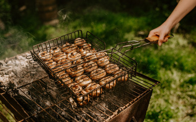 white identical small round mushrooms champignons stacked in even rows in a barbecue on the grill. Green grass background. Summer. White smoke over baked vegetables. 