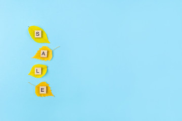 Word Sale. Wooden blocks with lettering and yellow leaves on blue background. Copy space, flat lay