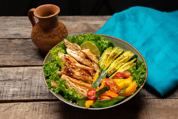 Grilled chicken salad with avocado and vegetables on wooden background