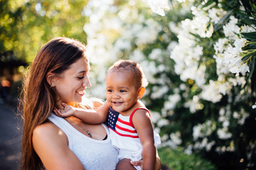 mother and daughter of different skin color smiling next to white flowers