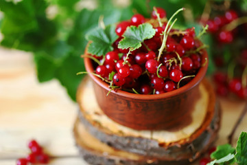Red currants in a bowl on a wooden background. Red currant leaves. Summer berries. Currant harvest.