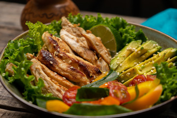 Grilled chicken salad with avocado and vegetables on wooden background