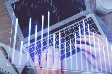 Double exposure of man's hands typing over computer keyboard and forex graph hologram drawing. Top view. Financial markets concept.