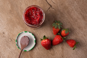 Glass of strawberry jam, spoon and strawberries over wooden table