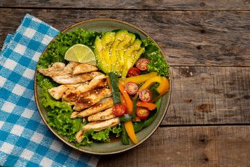 Grilled chicken salad with avocado and vegetables on wooden background